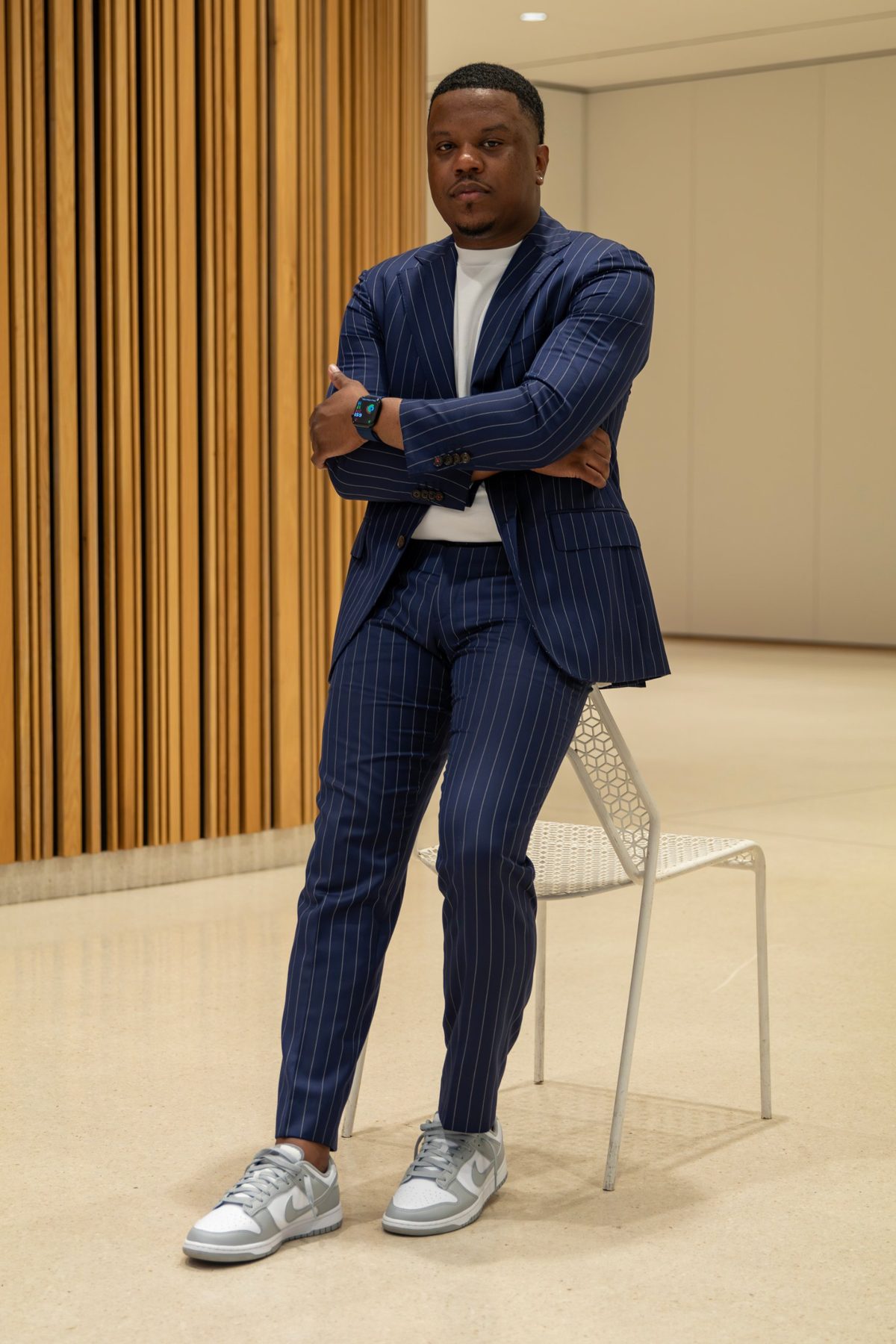 Darrell M. Robinson, Jr. in a navy pinstripe suit, arms crossed, leaning on a white chair